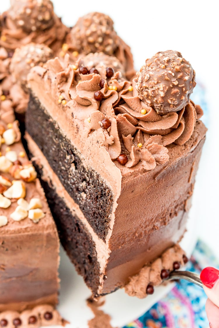 A slice of nutella cake being removed from the whole cake on a cake stand.