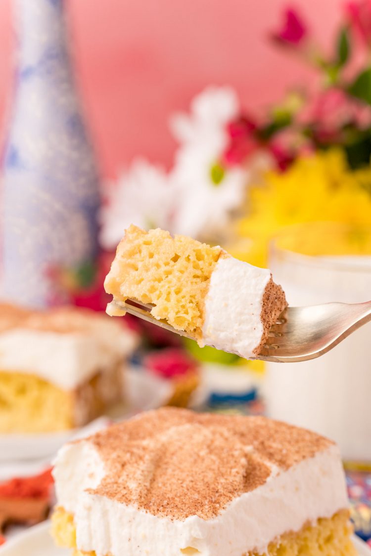 A fork with a bite or tres leche cake on it.