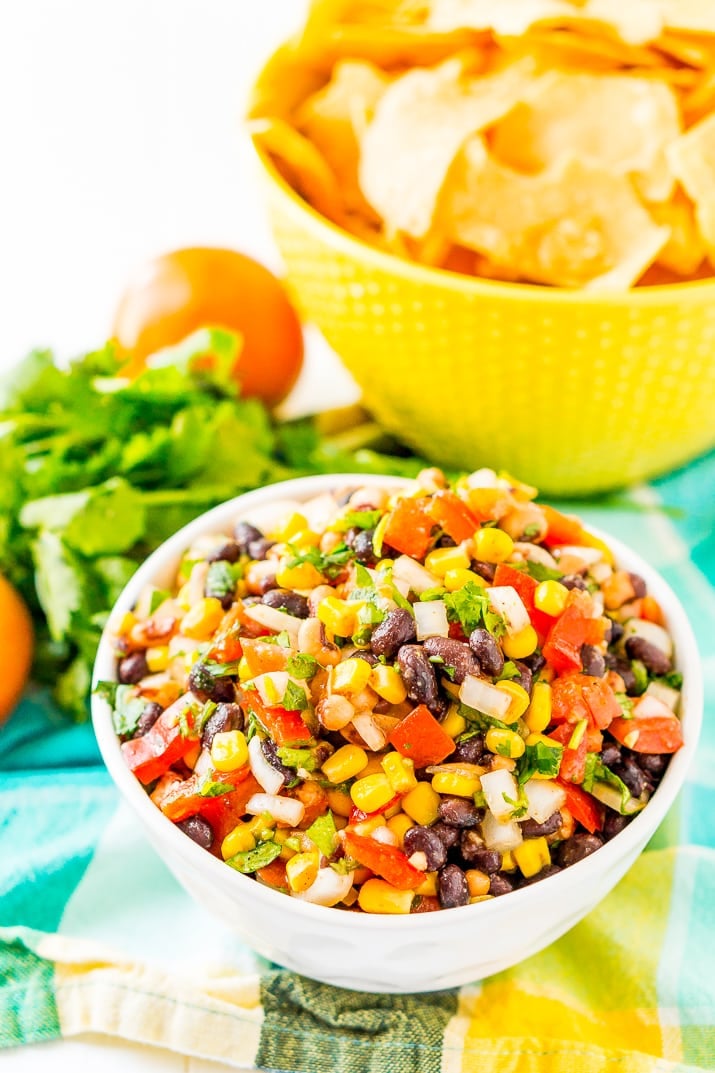 Bowl of Cowboy Caviar with a bowl of tortilla chips in background on teal and yellow napkin.