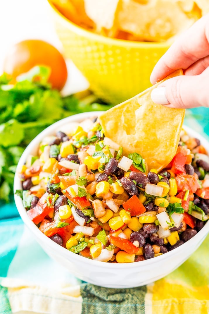 Woman's hand dipping a tortilla chip into a bowl of Cowboy Caviar.