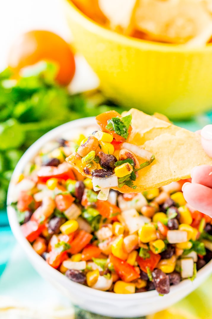 Woman's hand holding a tortilla chip with a scoop of Cowboy Caviar on it.