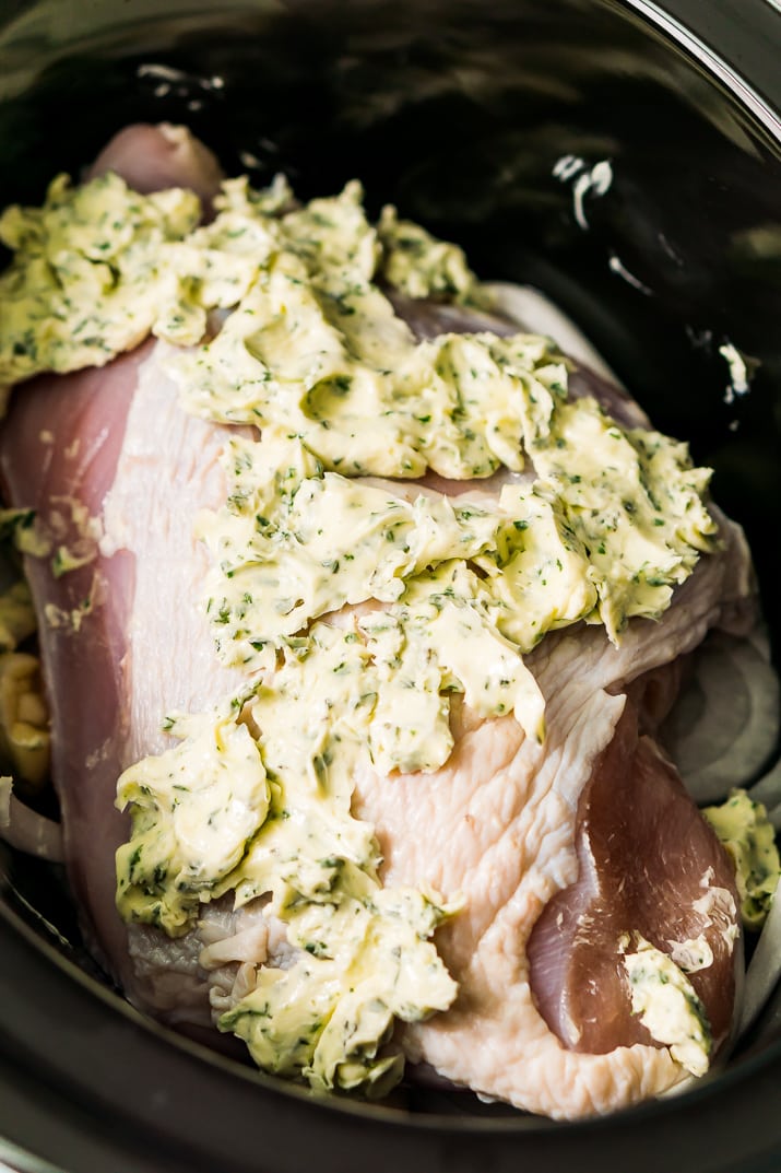 Turkey breast in a slow cooker covered in herb butter.