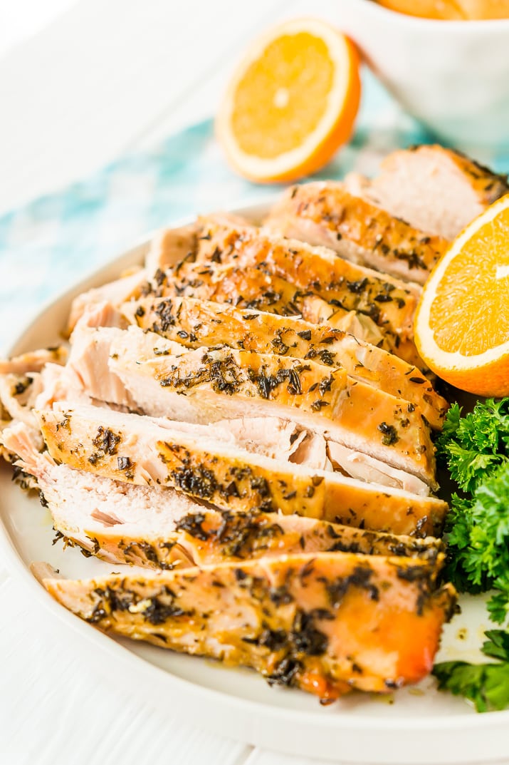Sliced Turkey Breast with herbs on a white plate with half an orange and parsley in the background.