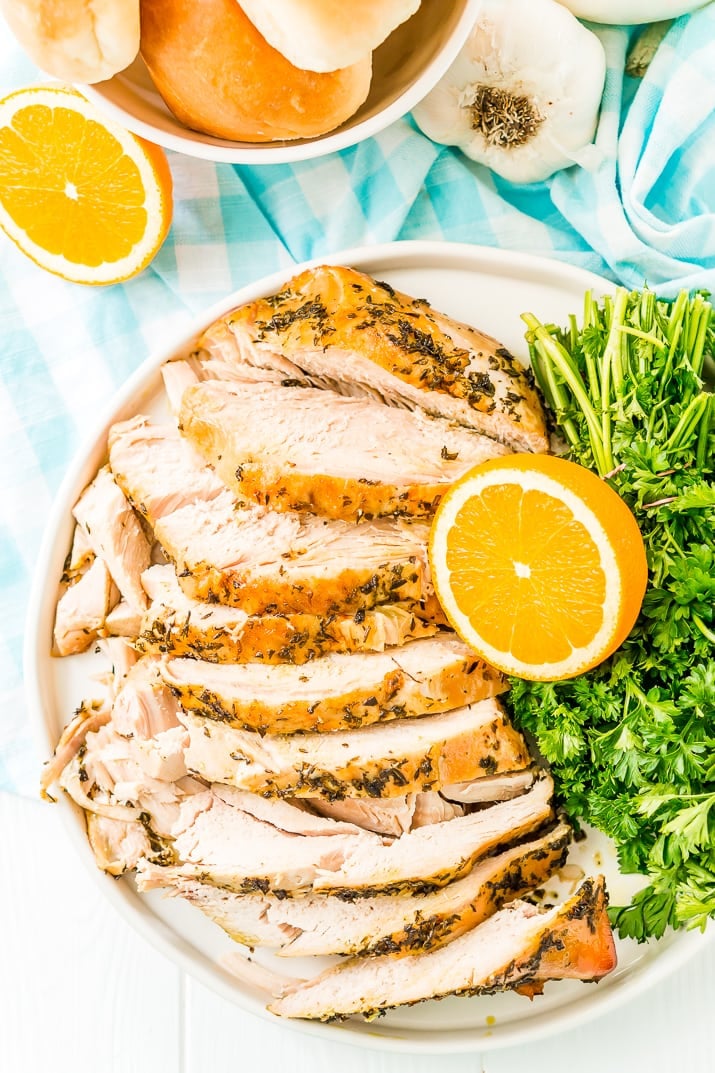 Overhead photo of a turkey breast covered in herbs and sliced on a plate with oranges and parsley.