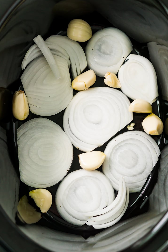 Onions and garlic in the bottom of a slow cooker.