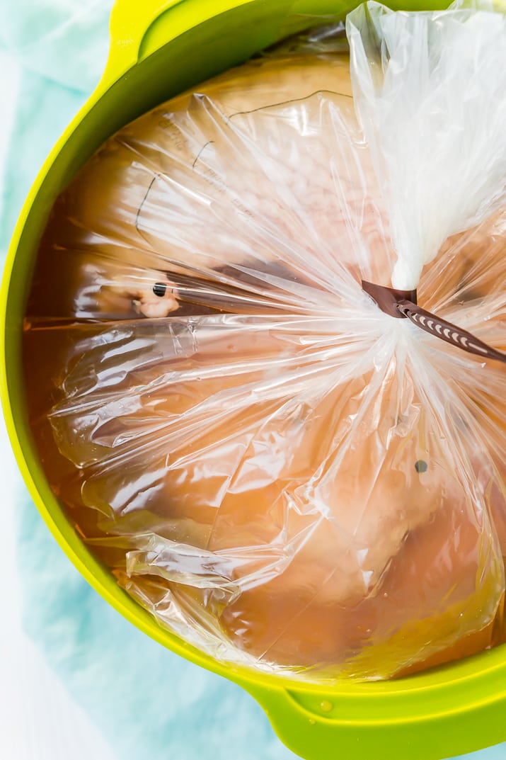 Turkey breast being brined in a plastic bag in a green bowl.