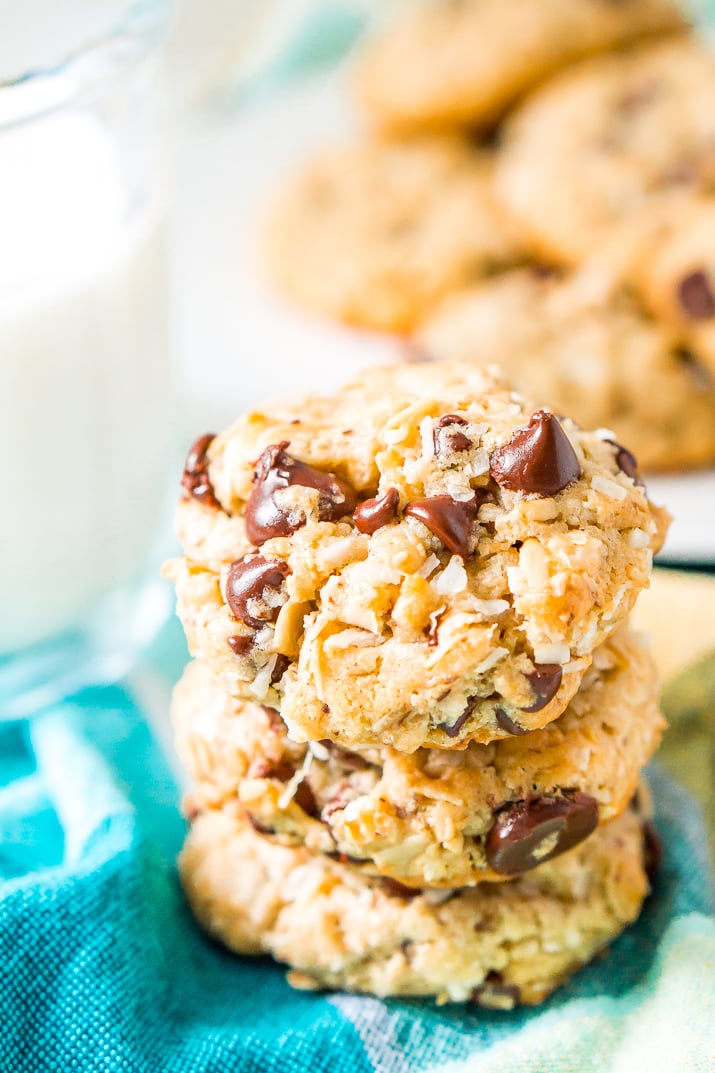 Three Lactation Cookies stacked on top of each other on turquoise napkin with milk and plate of cookies in the background.