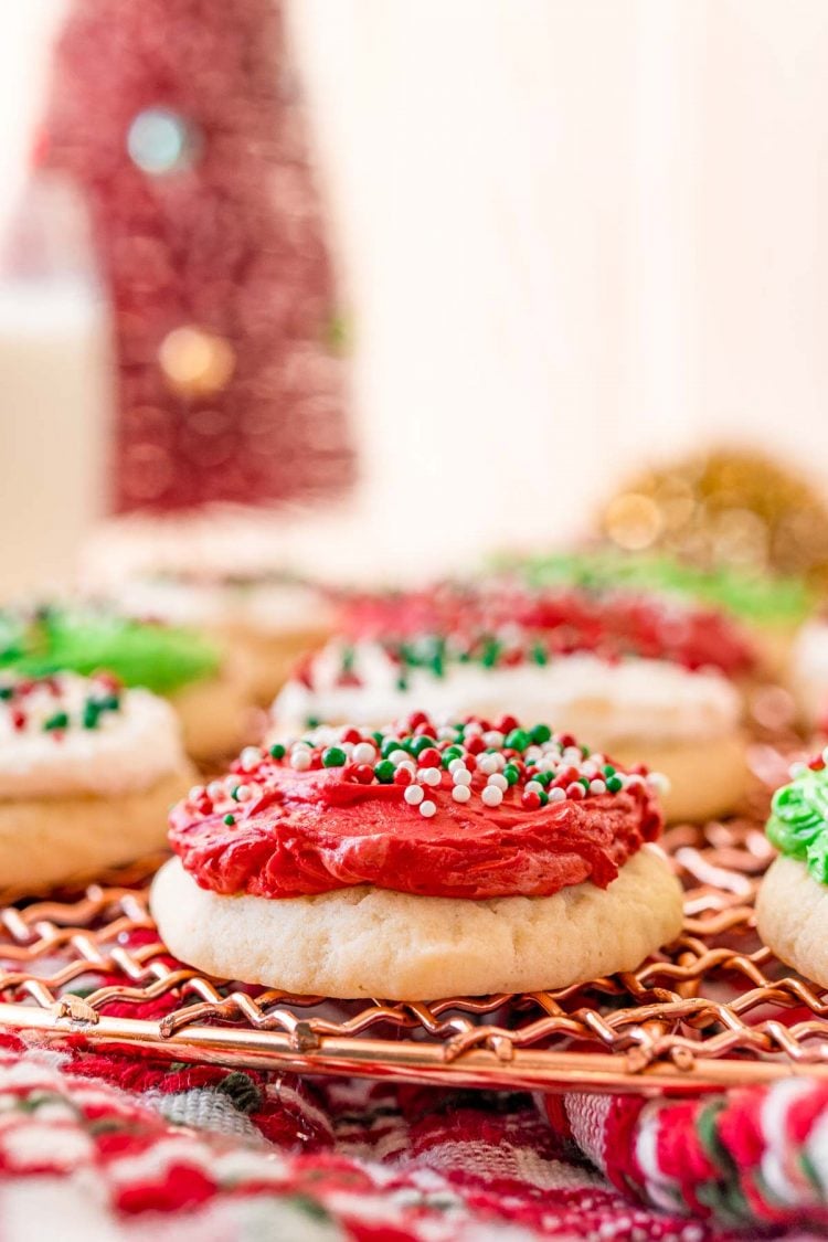 Close up photo of a red frosted sugar cookies with more green and white frosted cookies in the background.