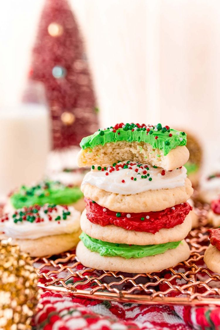 A stack of round sugar cookies on a copper wire rack with the top one missing a bite.