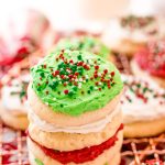 A stack of red, white, and green frosting sugar cookies on a cooling rack surrounded by holiday decorations.