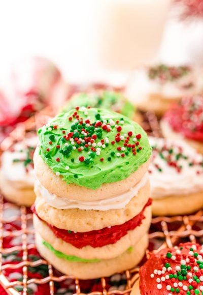 A stack of red, white, and green frosting sugar cookies on a cooling rack surrounded by holiday decorations.
