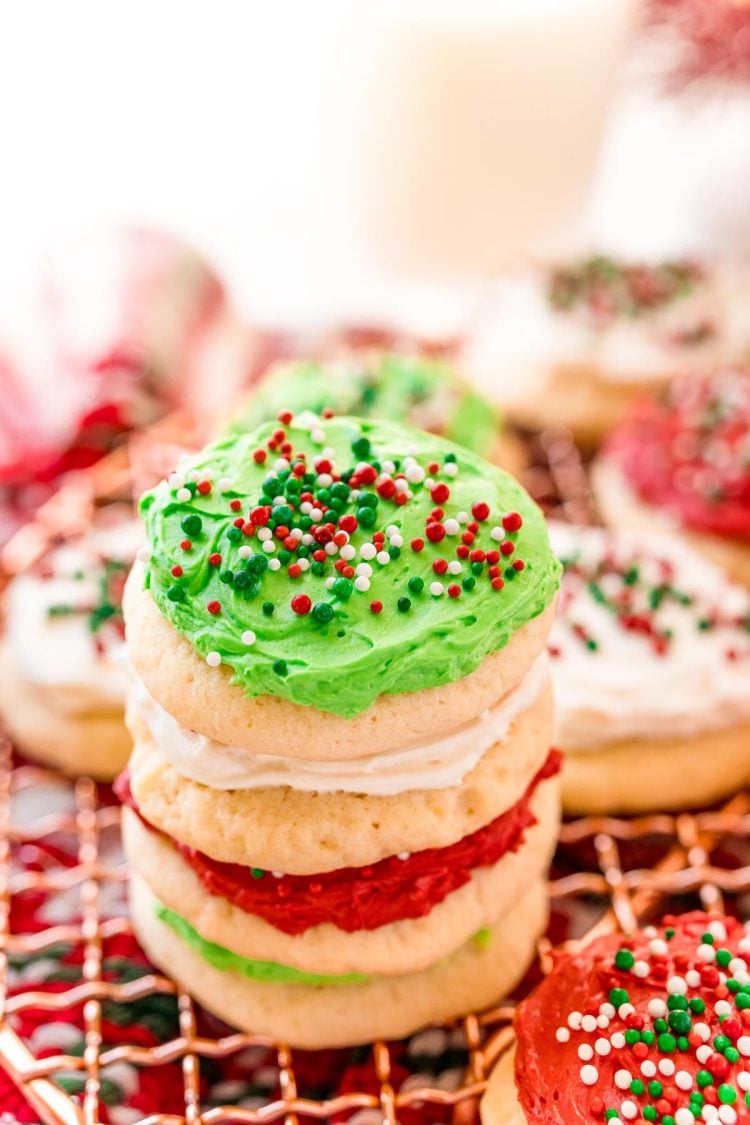 A stack of red, white, and green frosting sugar cookies on a cooling rack surrounded by holiday decorations.