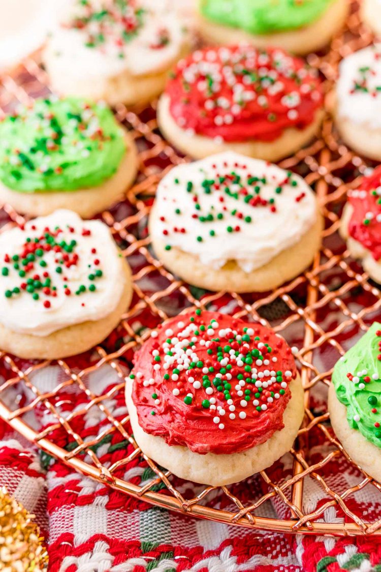 Red, white, and green frosted sugar cookies on a wire cooling rack covered in sprinkles.