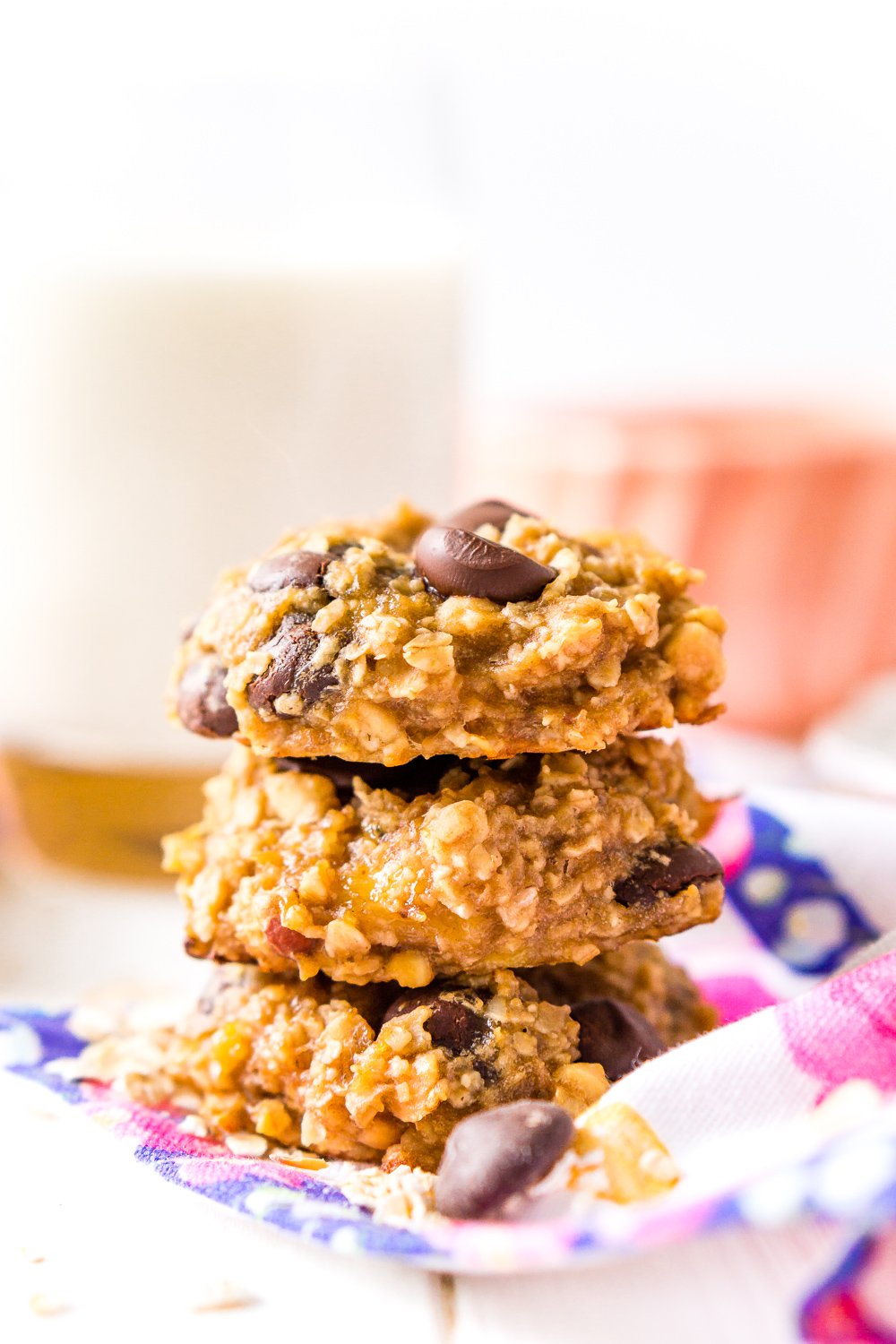 Banana Oatmeal Cookies with chocolate chip stacked three high with milk in background.