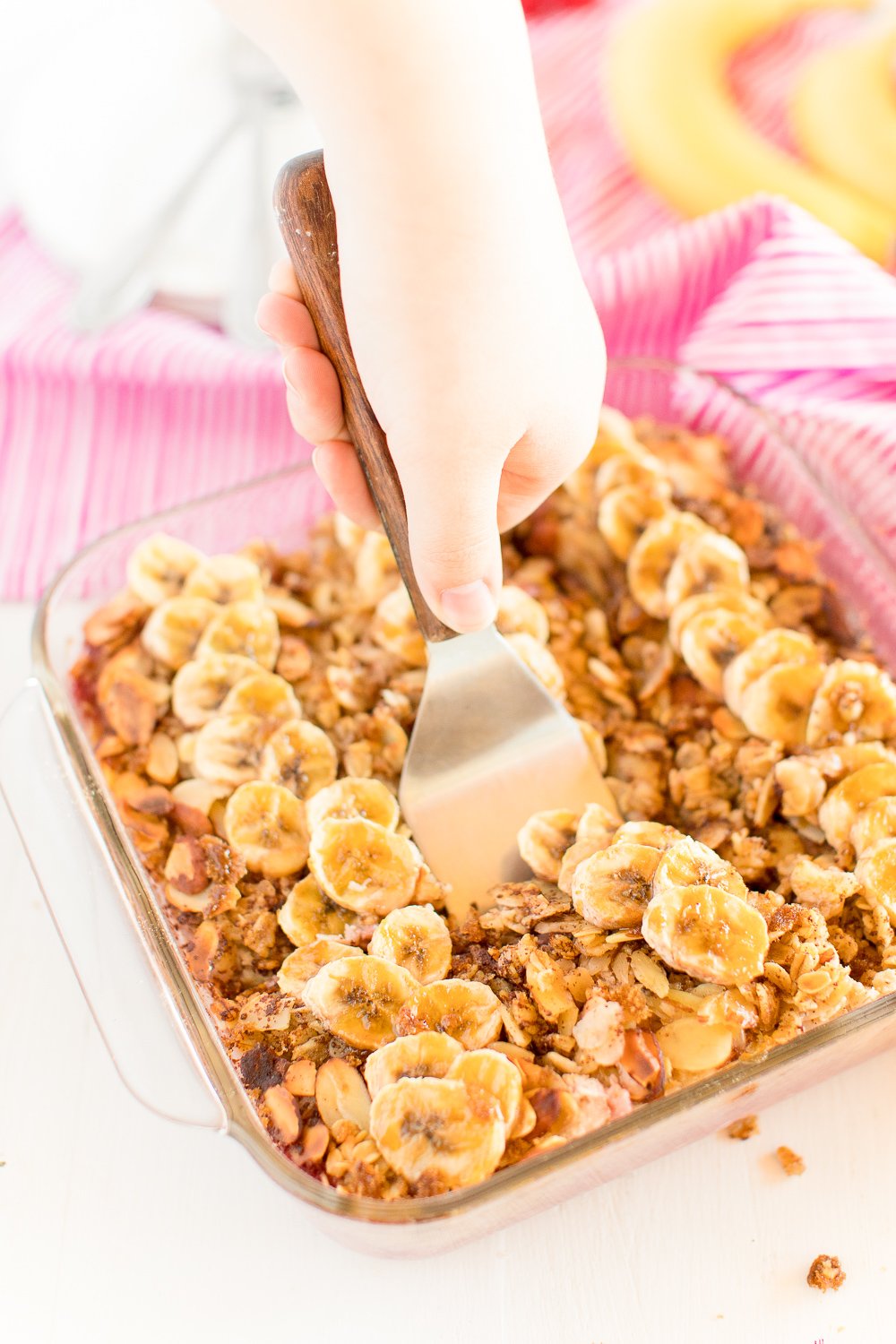 Woman's hand using a spatula to scoop baked oatmeal out of baking dish.