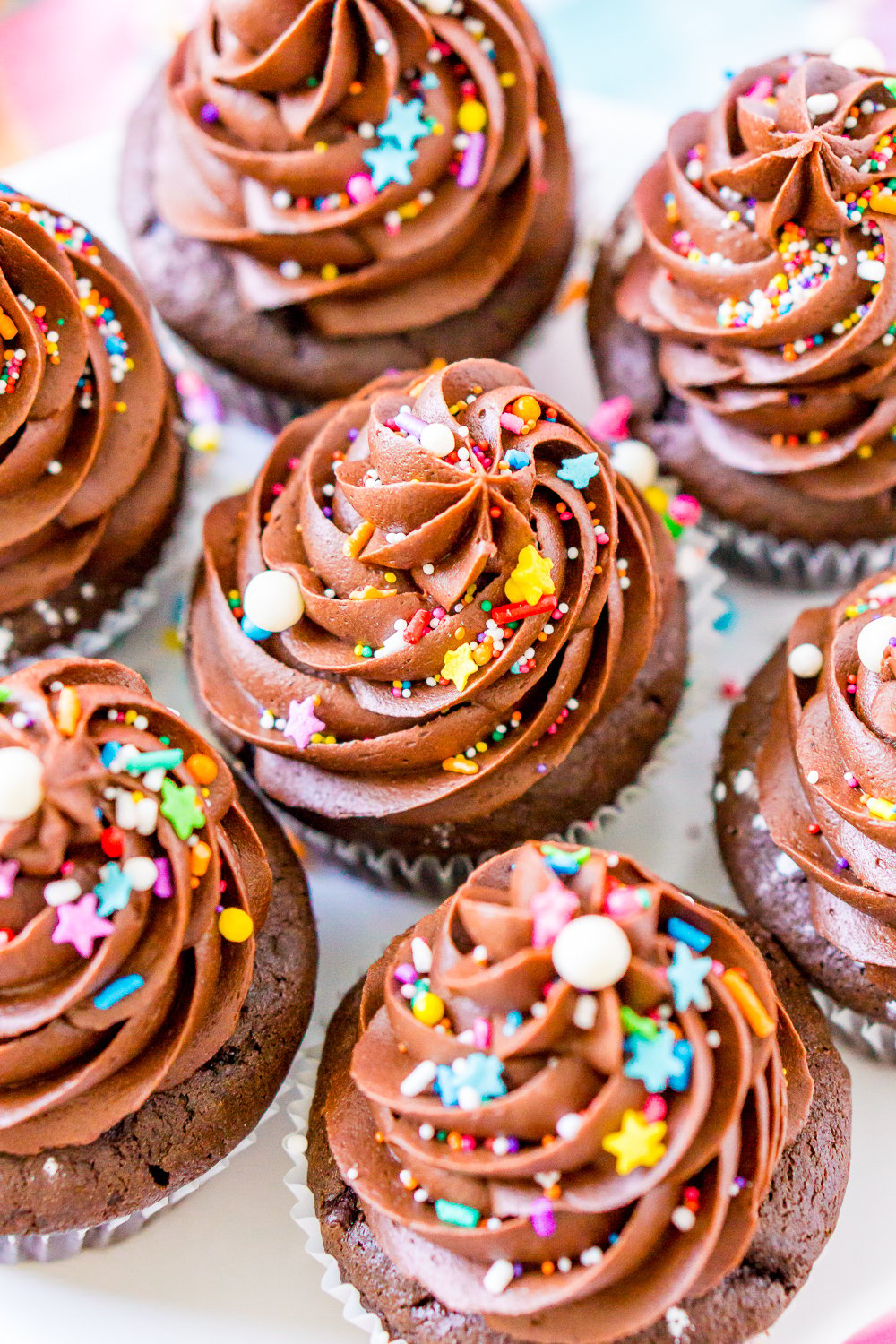 Chocolate Buttercream Frosting on chocolate cupcakes on white cake stand with colorful sprinkles.