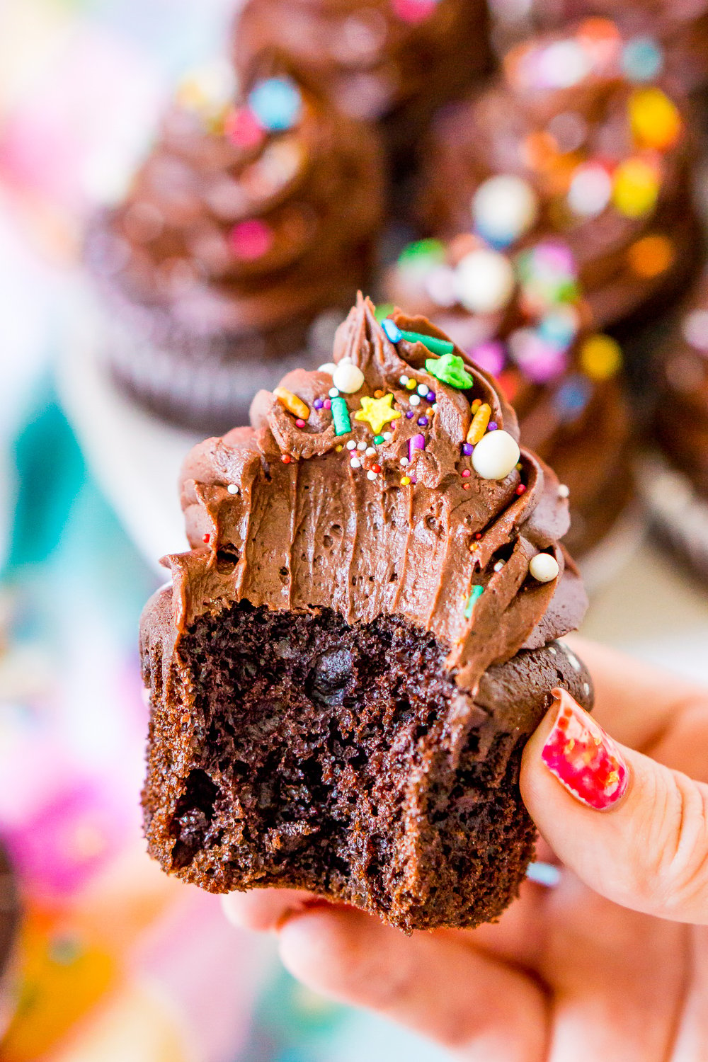 Woman's hand holding a chocolate cupcake with a bite taken out of it.