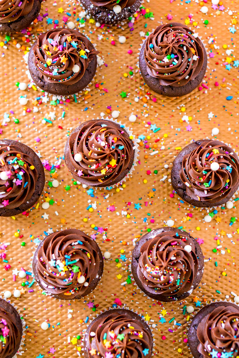 Chocolate Cupcakes on a copper baking sheet with sprinkles scattered around.