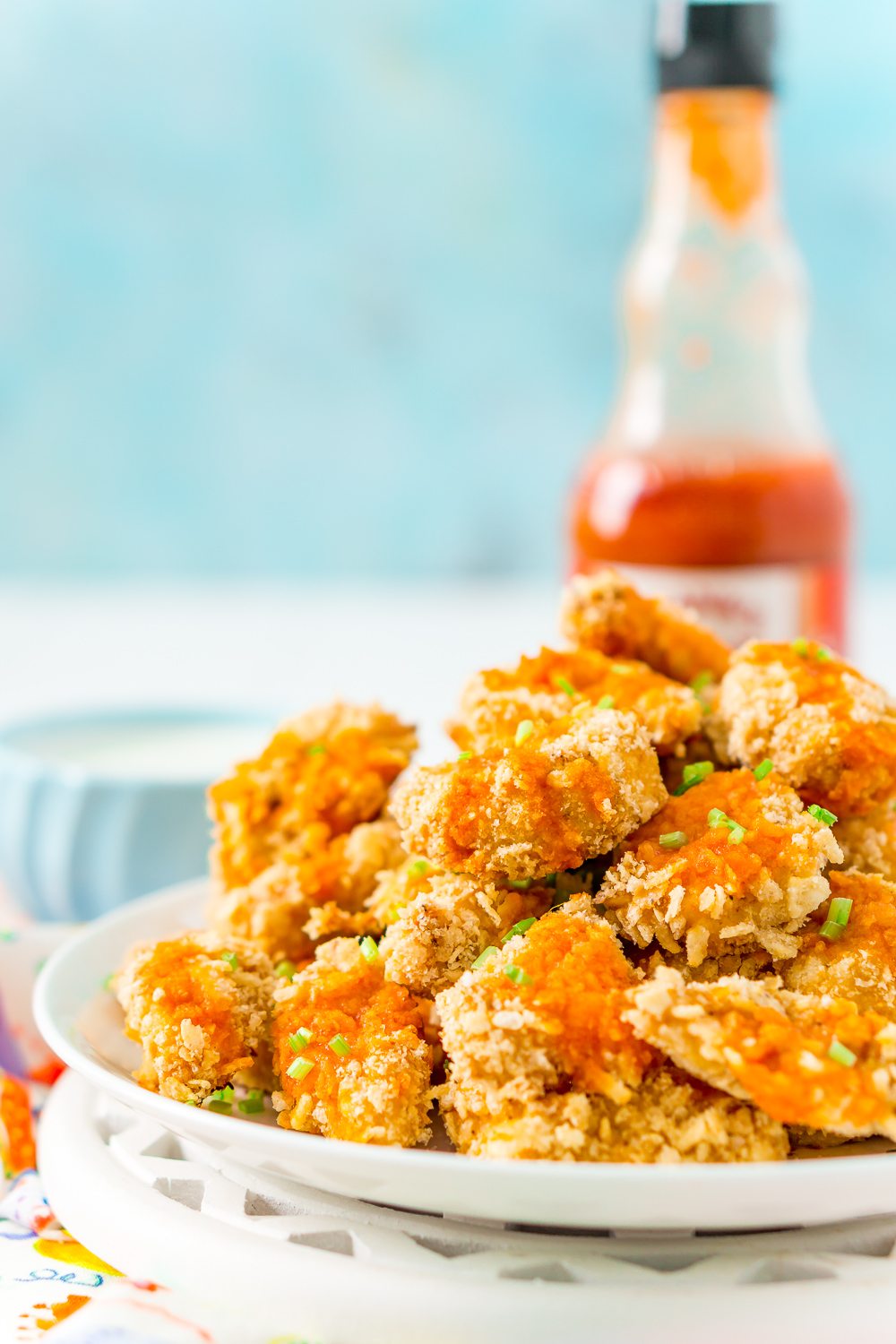 Plate of crispy baked chicken wings with hot sauce bottle in background and blue wall background.