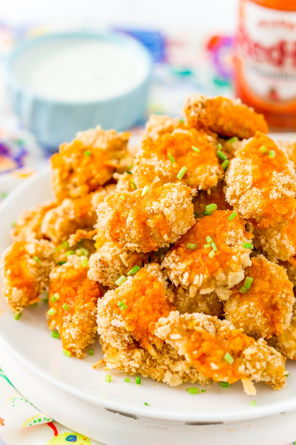 Crispy Baked Chicken Wings on a white plate with dipping sauce and hot sauce bottle in the background.