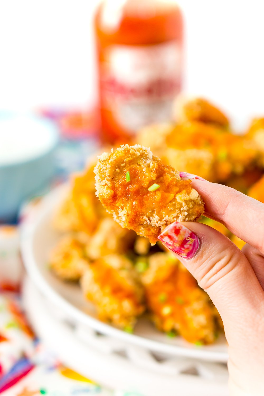 Woman's fingers holding Crispy Baked Chicken wing with buffalo sauce.