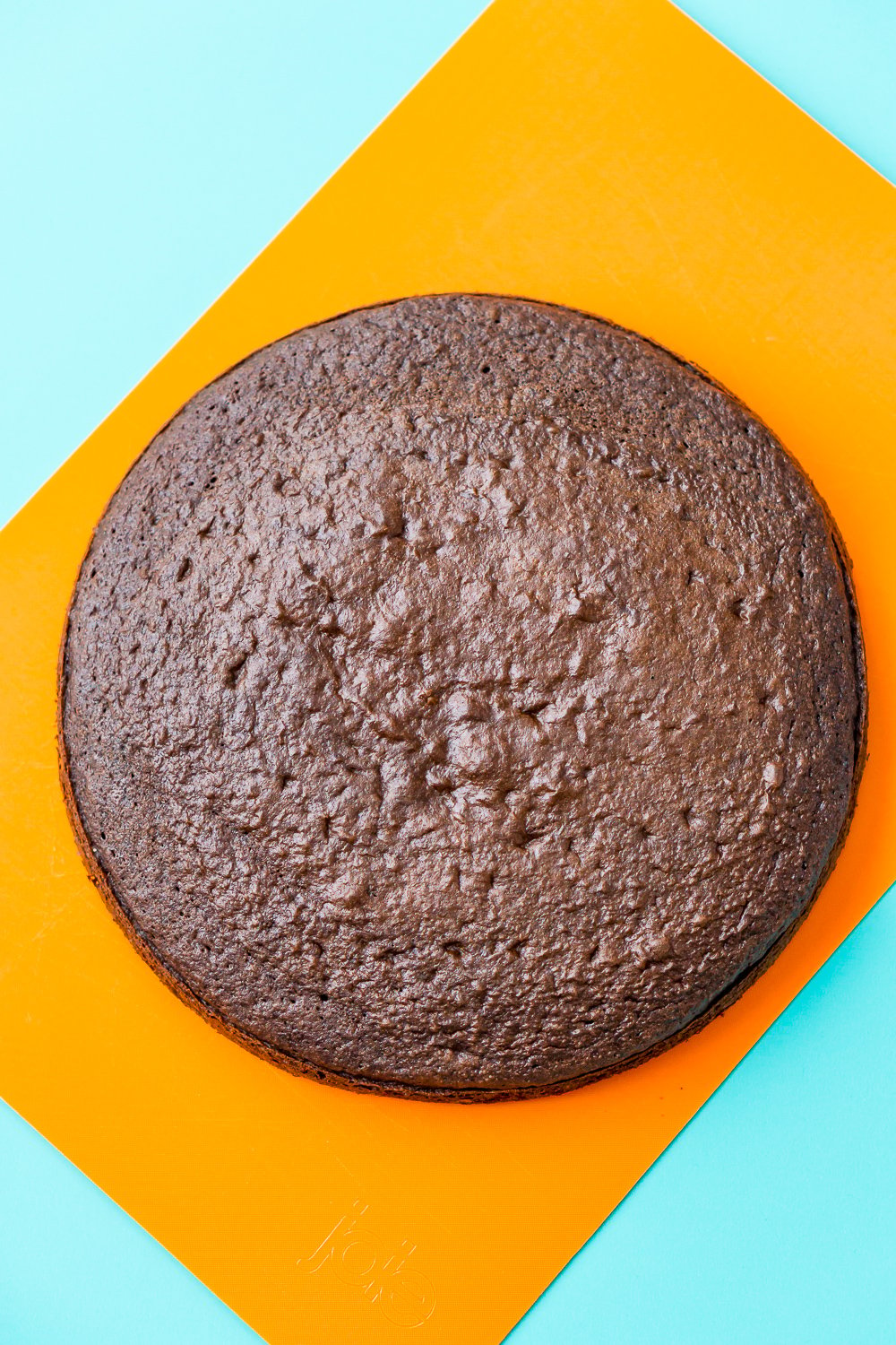 A round chocolate cake layer without frosting on an orange cutting board. 