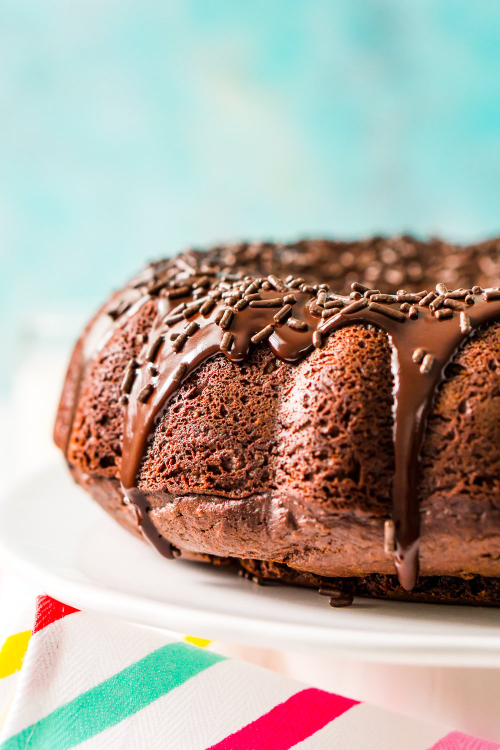 Healthy Chocolate Bundt Cake on white cake stand with blue background and striped napkin.