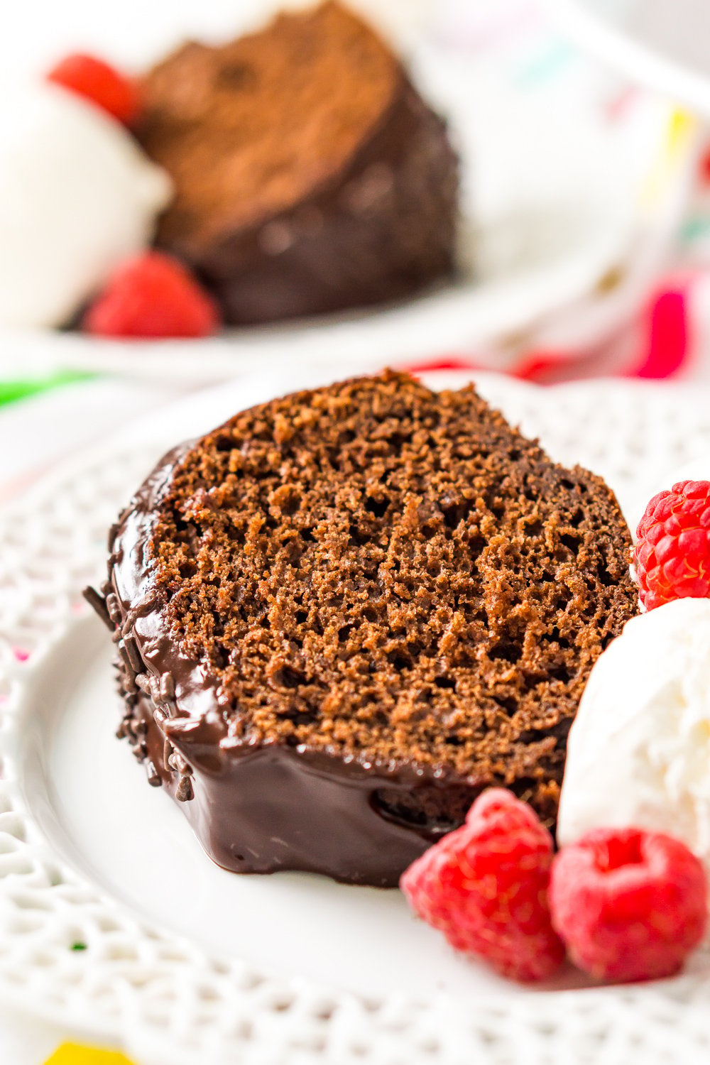 Slice of Chocolate Yogurt Cake on white plate with ice cream and raspberries.