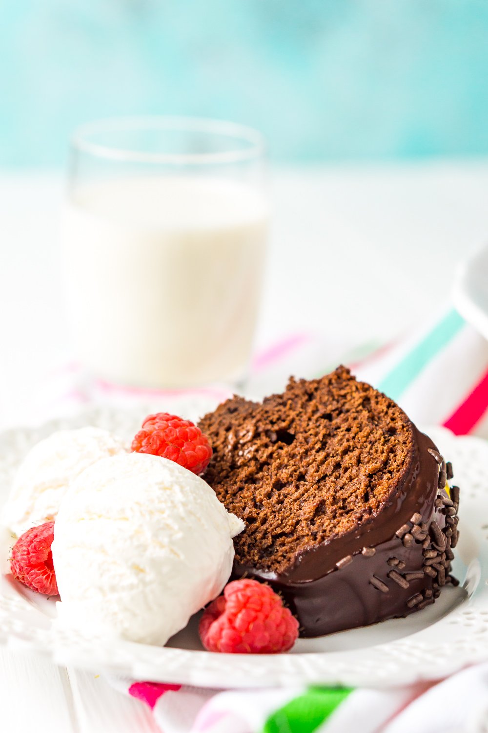 Slice of healthy chocolate cake on white plate with ice cream and fresh raspberries served with a glass of milk.