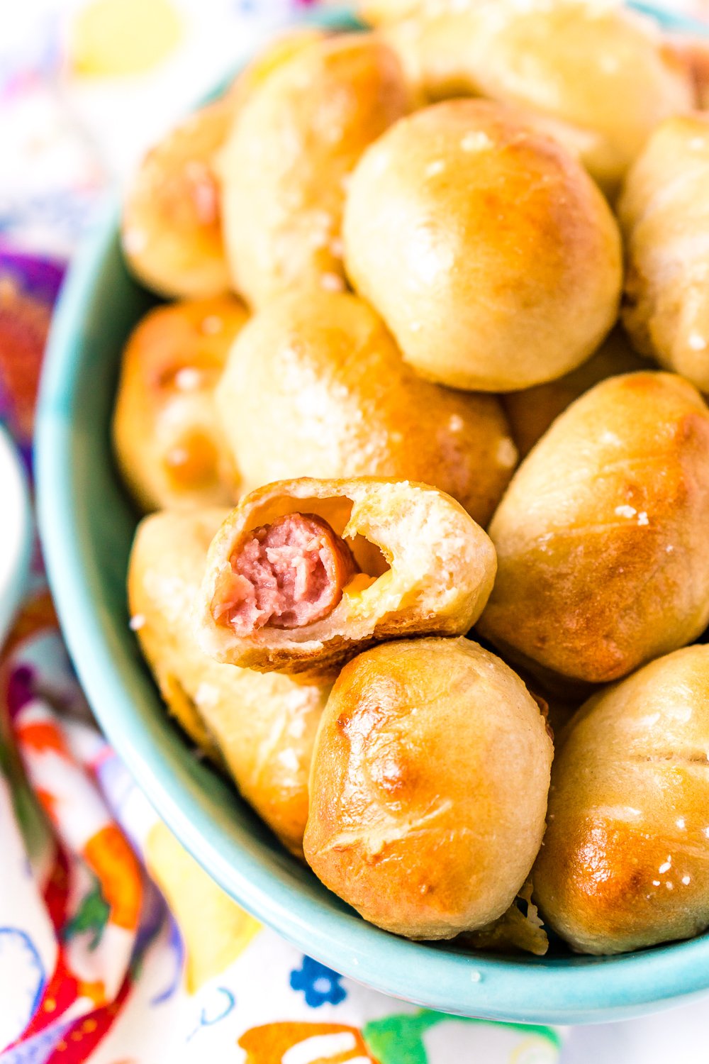 Bowl of pretzel pigs in a blanket with bite taken out of one.