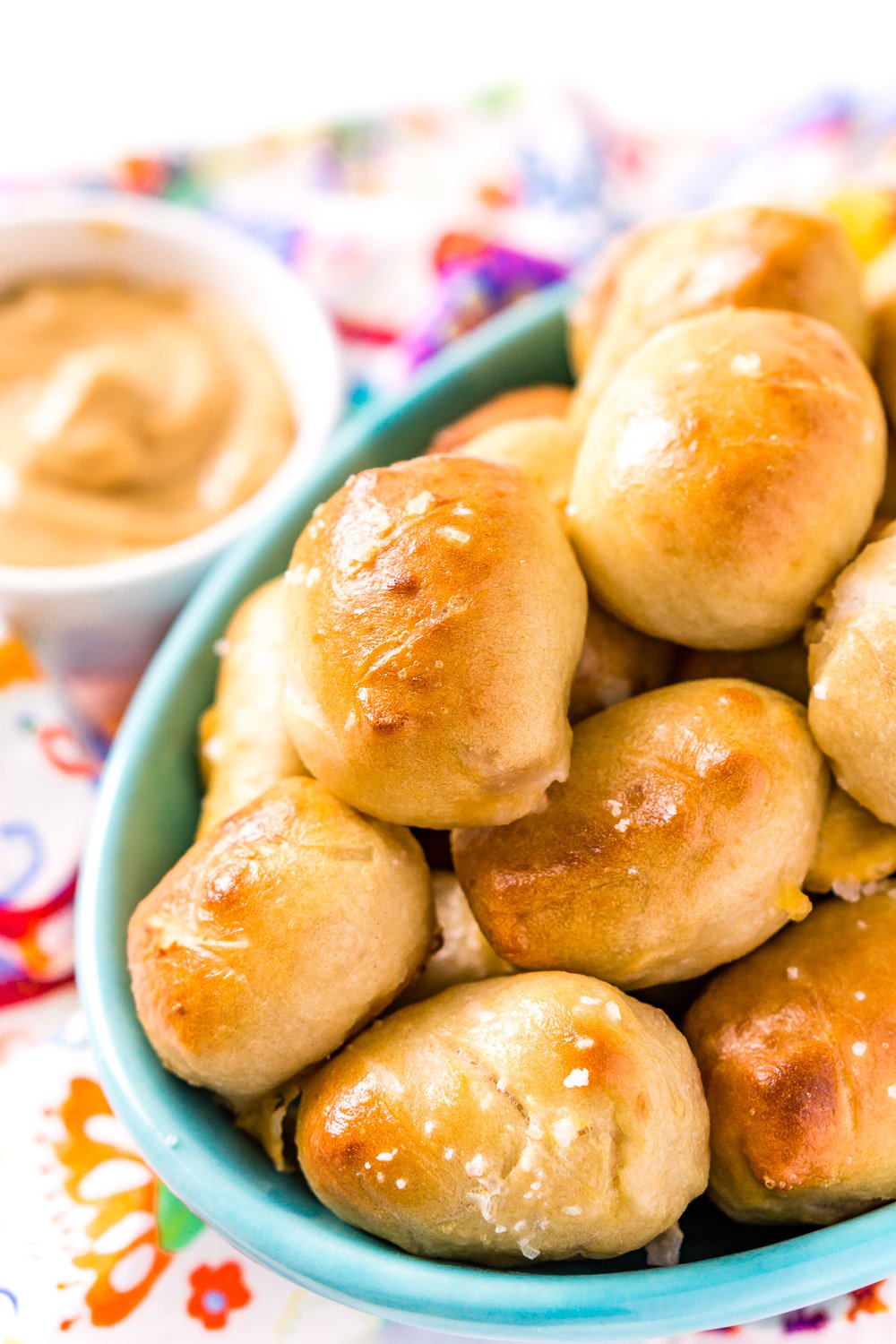Pretzel Pigs In A Blanket in a teal bowl with dipping sauce in the background.
