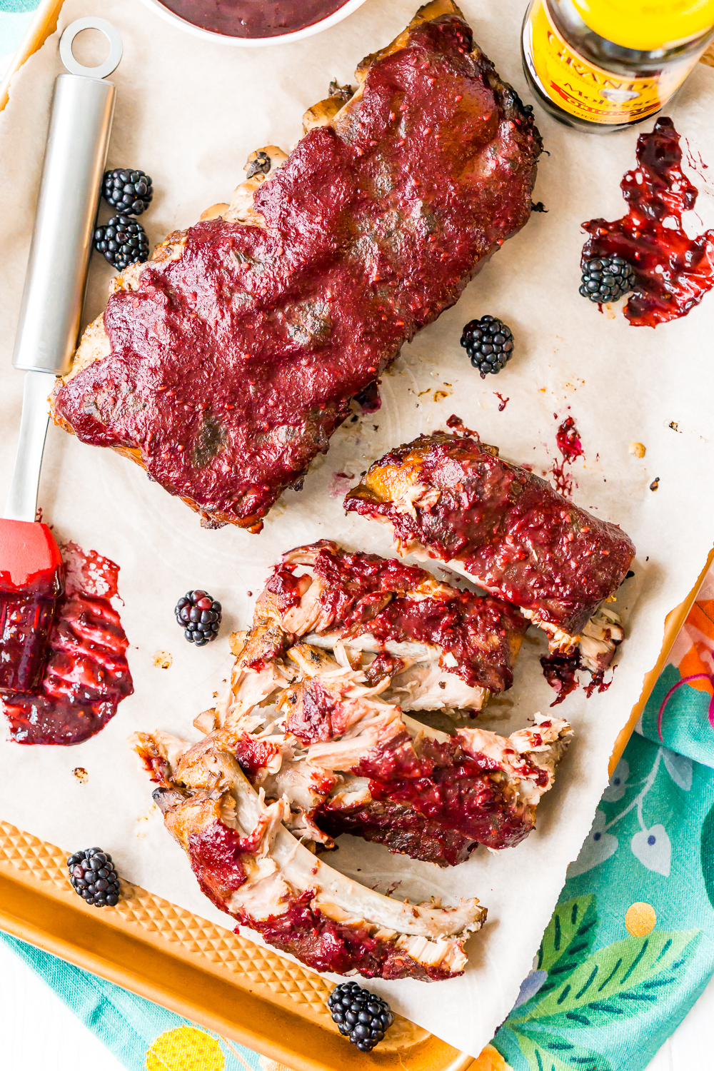 Overhead photo of baby back ribs on sheet pan with blackberries and basting brush.