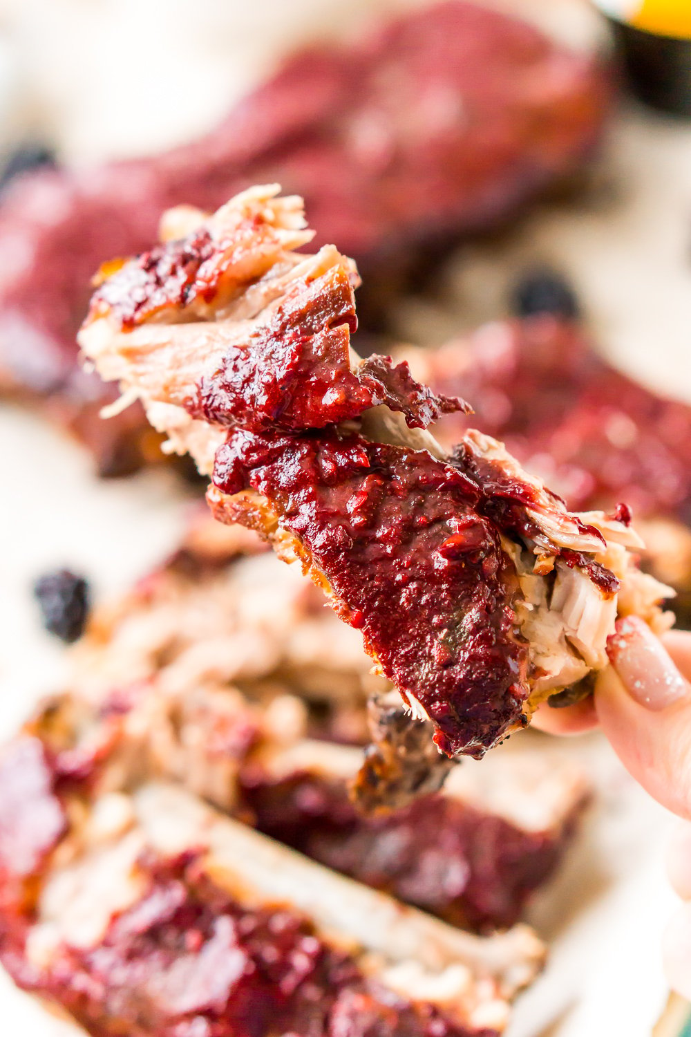 woman's hand holding baby back rib with blackberry barbecue sauce on it.