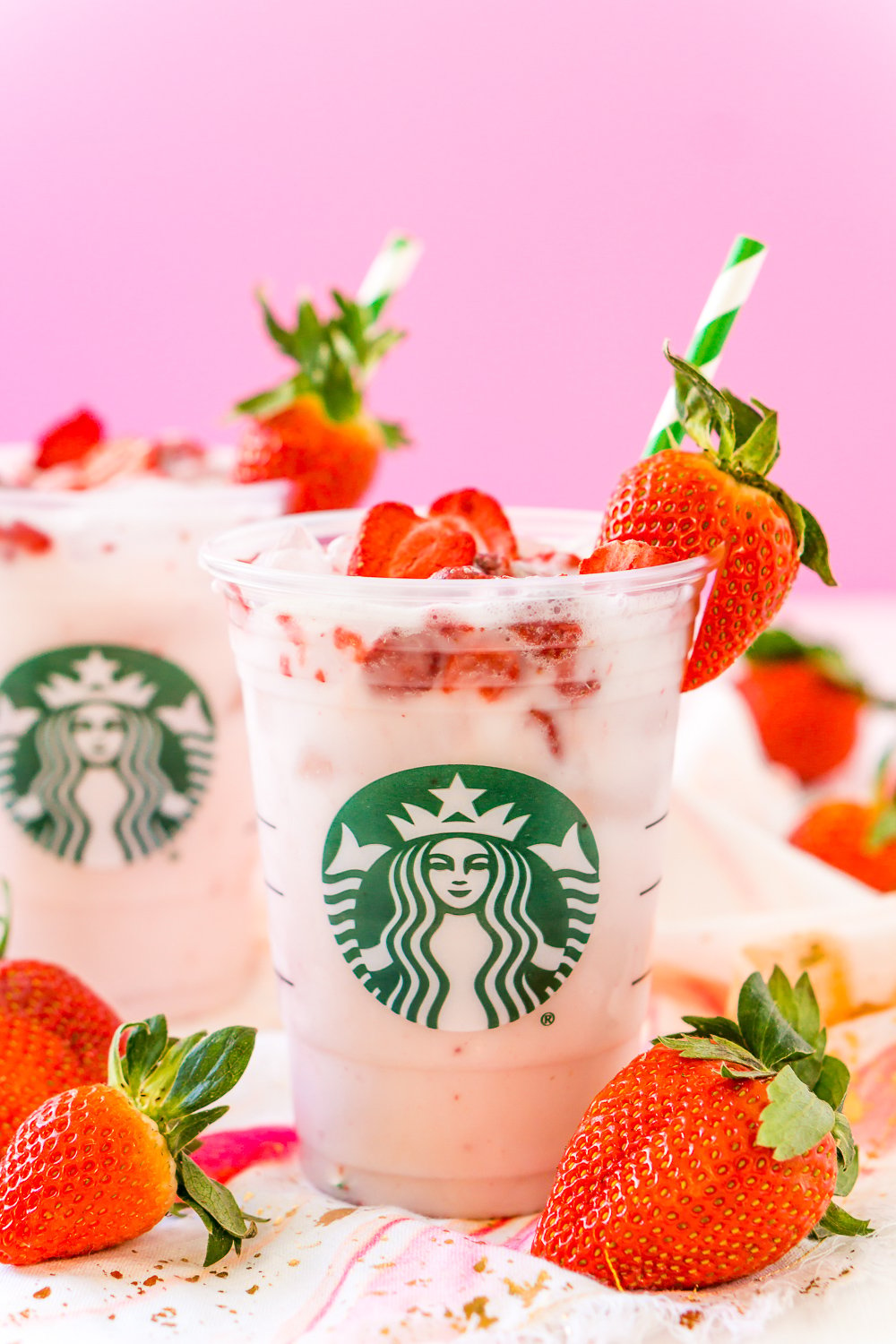 Copycat Starbucks Pink Drink in clear Starbucks cup with strawberries and pink background.