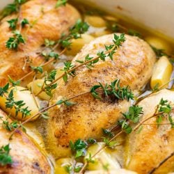 Close up photo of chicken breasts, garlic, thyme, and olive oil in a baking dish.