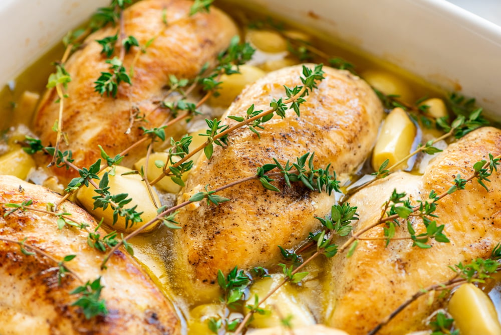 Close up photo of chicken breasts, garlic, thyme, and olive oil in a baking dish.