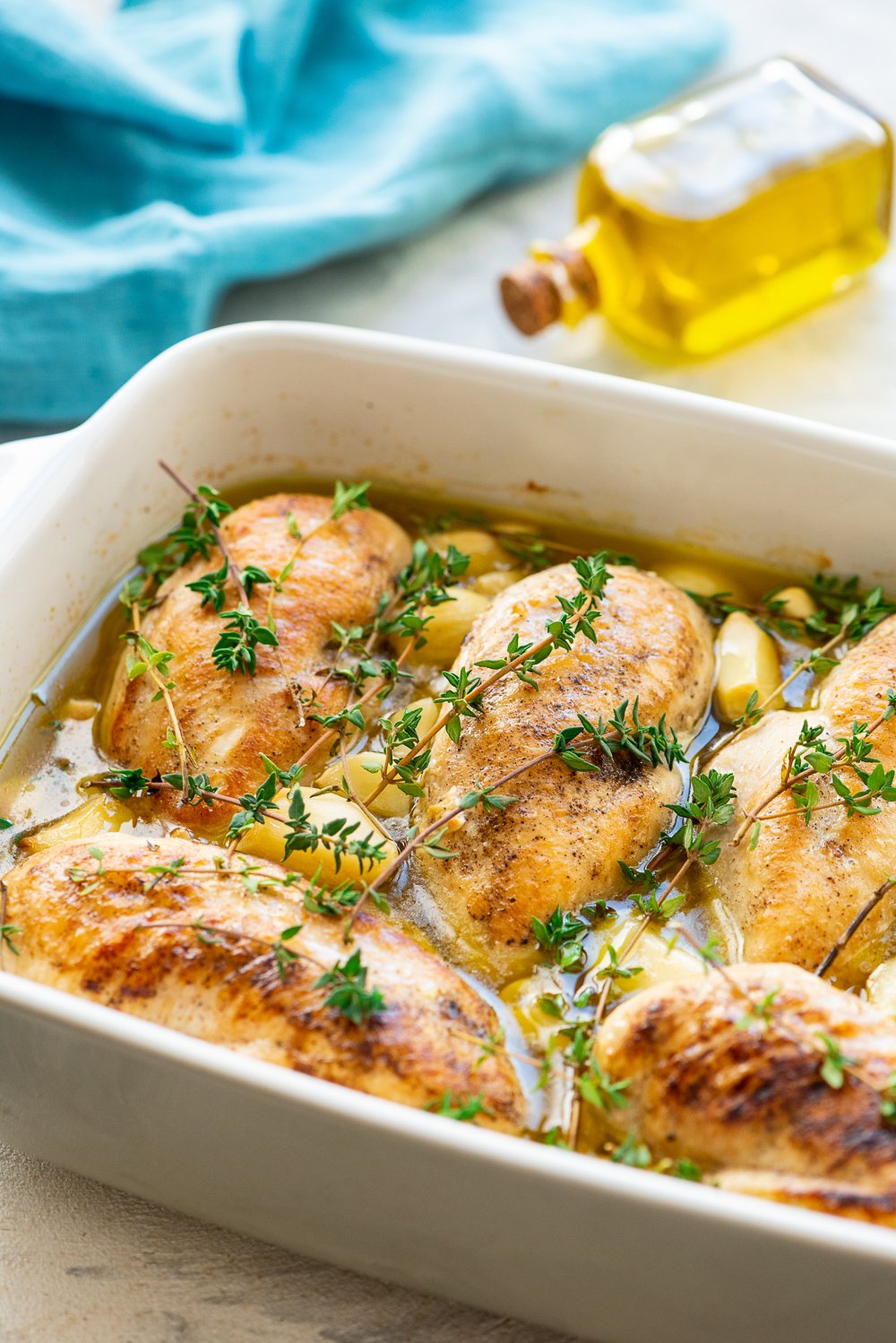 Garlic Chicken in a white baking dish with olive oil bottle and blue napkin in background.