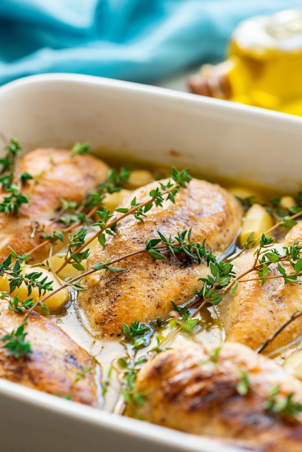 Baked Garlic Chicken in baking dish with thyme and garlic cloves.