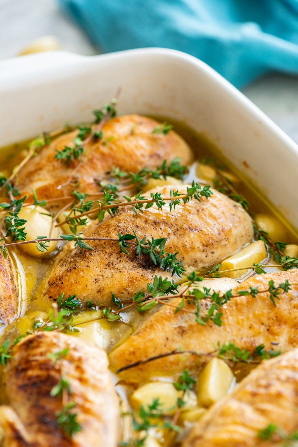 Roasted Garlic Chicken in a white casserole dish with blue napkin