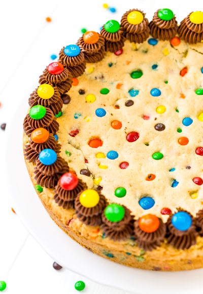This M&M's Cookie Cake Recipe is a fun and easy dessert recipe the whole family will enjoy. A giant cookie made with M&M's and chocolate frosting for even more deliciousness!