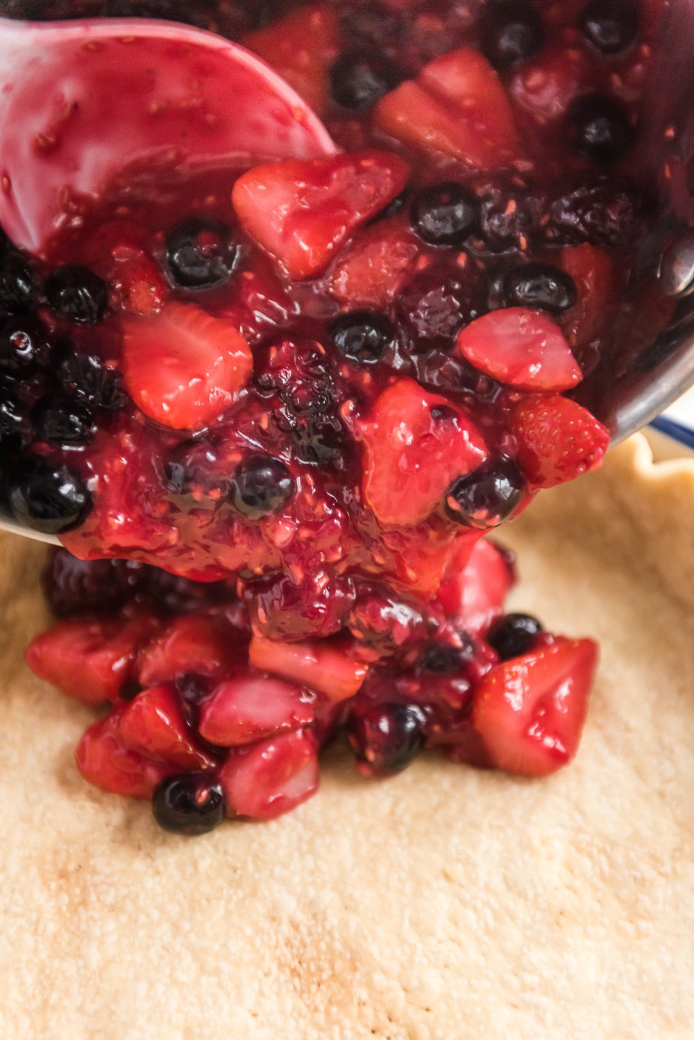 Mixed Berry Pie filling being poured into a prepared pie crust.