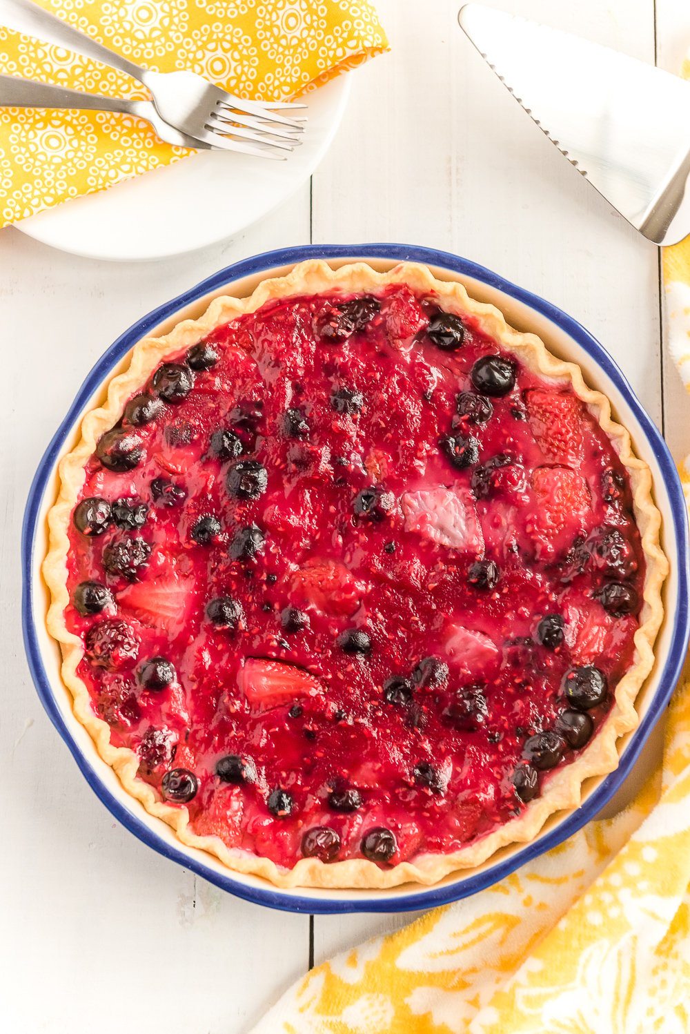 Overhead shot of a whole Mixed Berry Pie on white wood table.