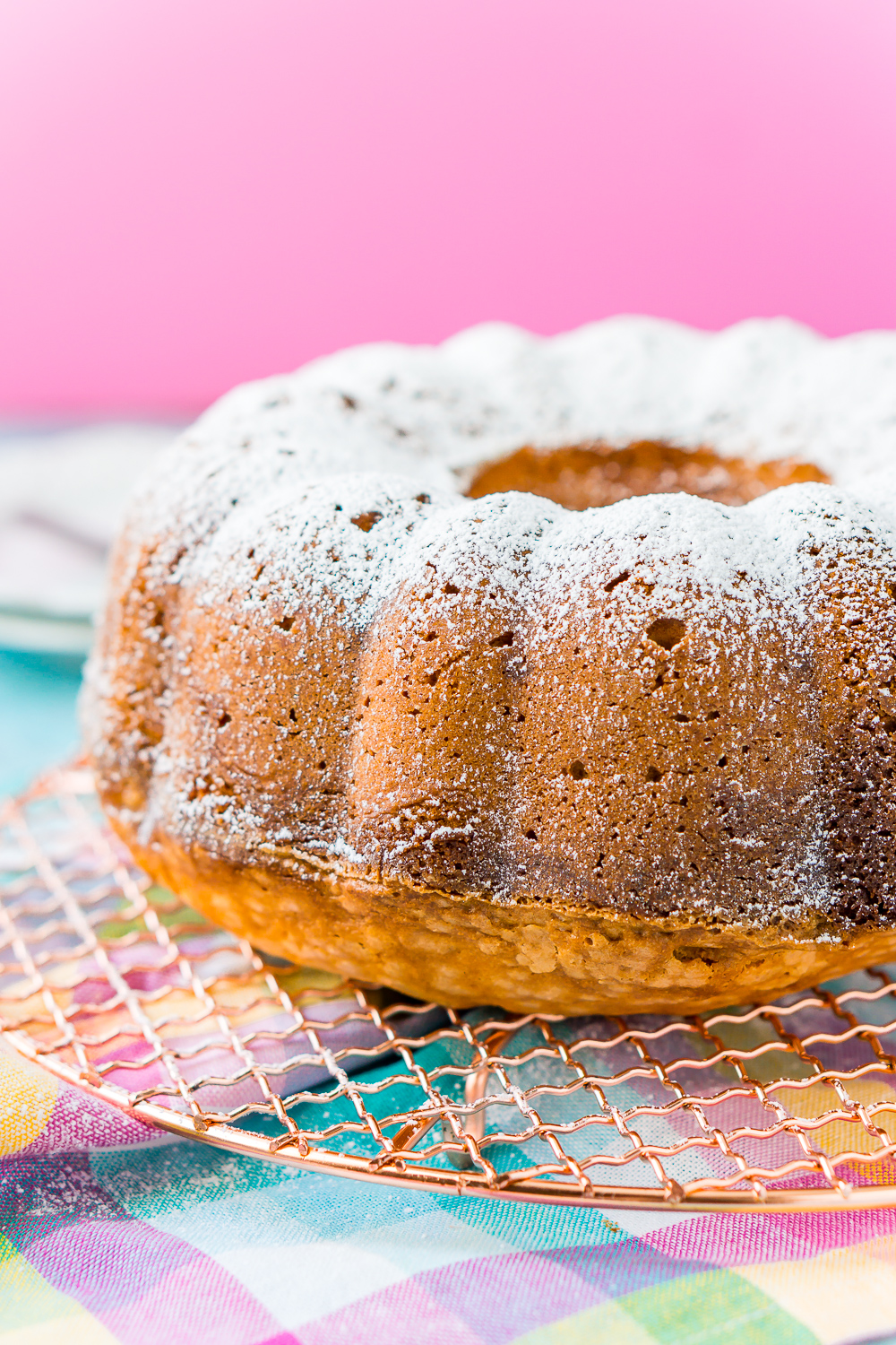 Cream Cheese Pound Cake on cooling rack with colorful napkin underneath and pink background.