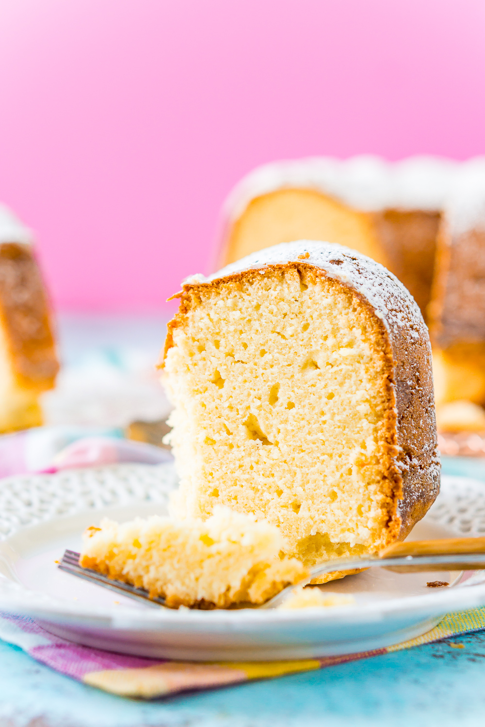 Slice of Cream Cheese Pound Cake on a white plate with a bite taken out of it on a fork resting on the plate.