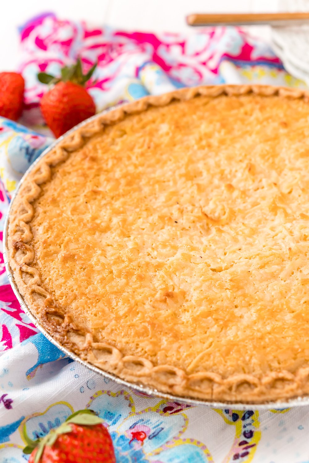 Photo of a Coconut Custard Pie in a pie tin with strawberries scattered around.