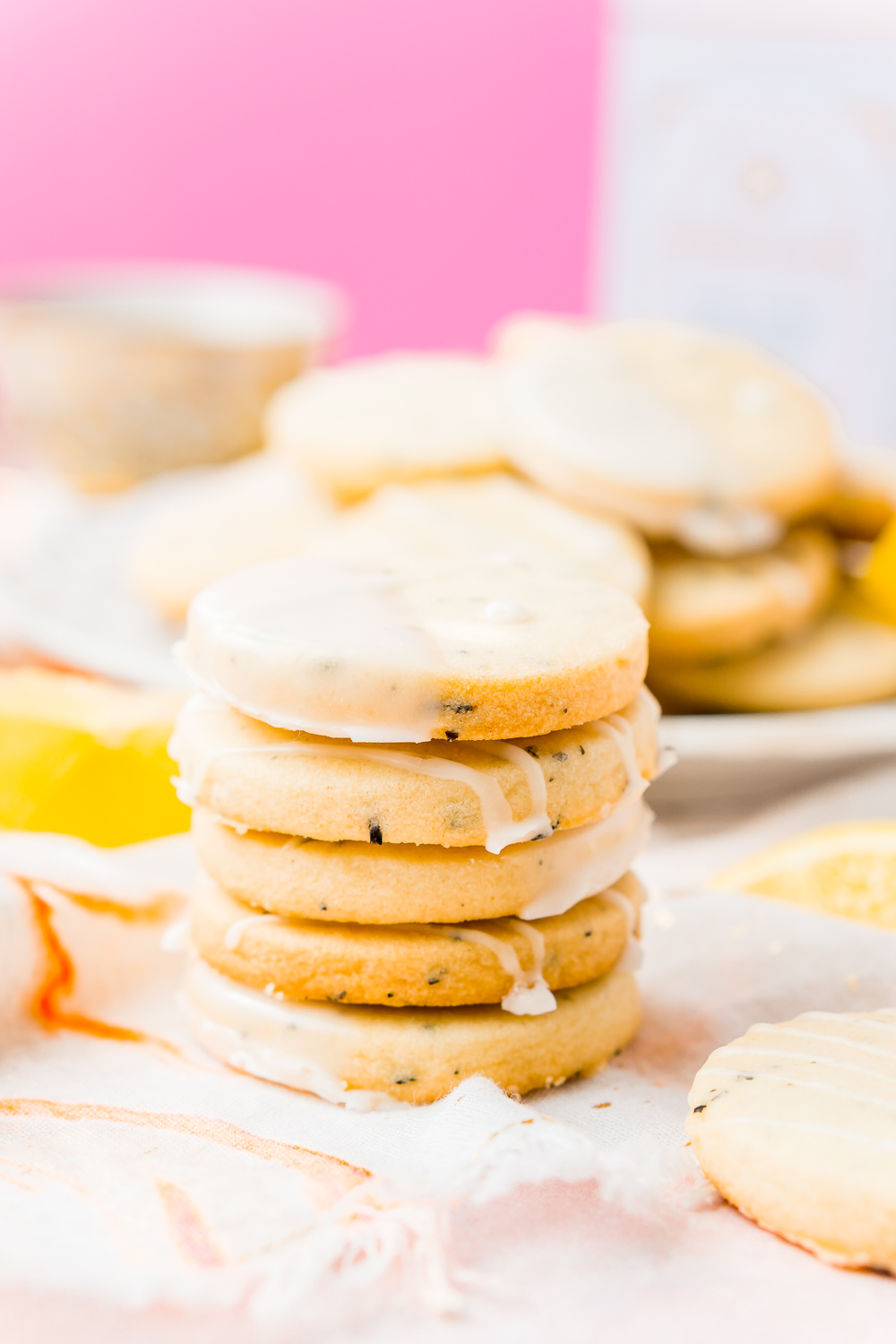 Stack of five Earl Grey Cookies with lemon icing with plate of cookies in the background.