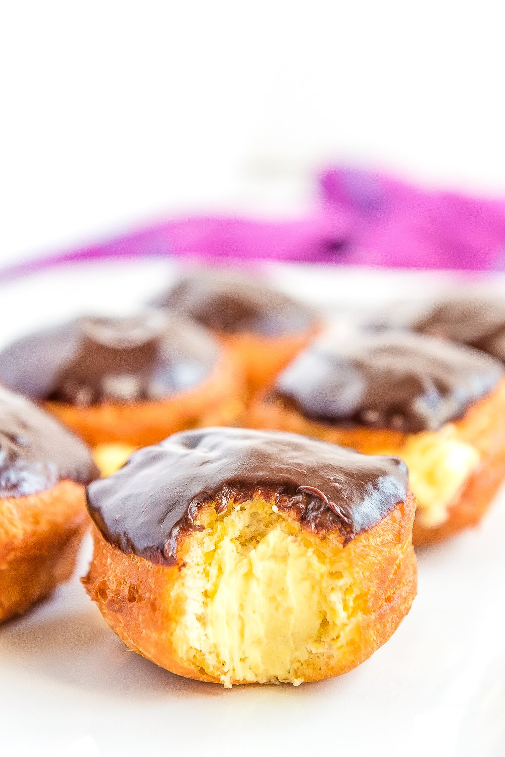 Boston Cream Donuts on a white plate. One has a bite taken out of it.