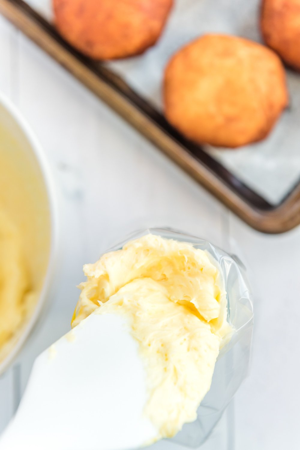 Pastry cream being added to a plastic piping bag with a white rubber spatula.