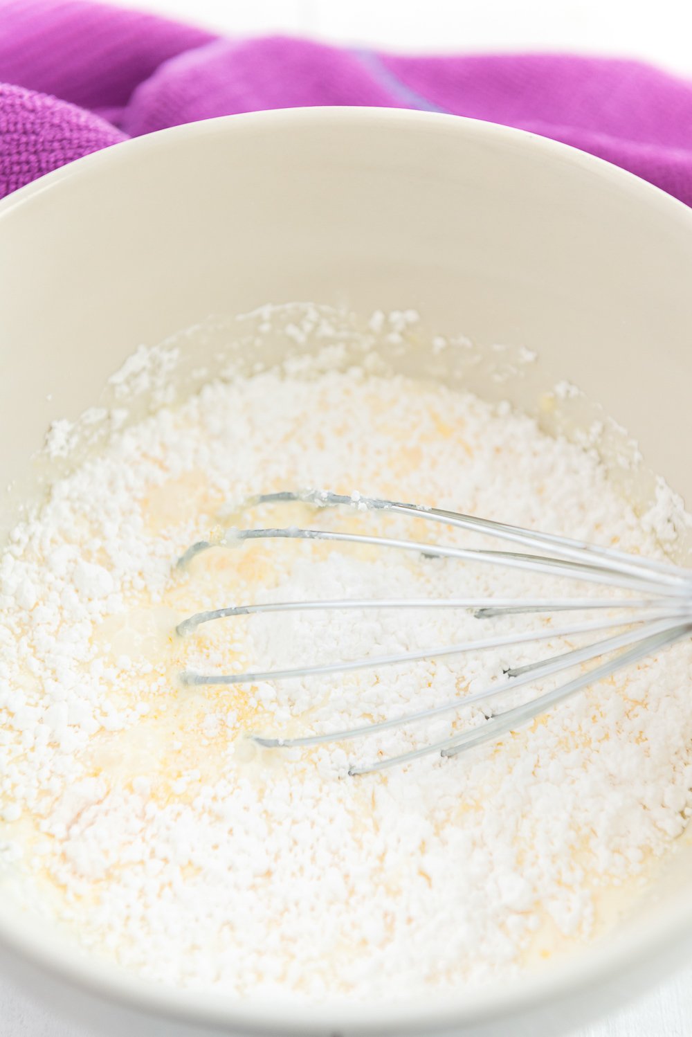 Heavy cream, sugar, and other pastry cream ingredients being mixed in a white bowl.