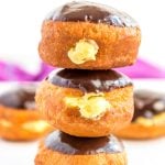 Stack of three Boston Cream Donuts on top of each other, more donuts in background.